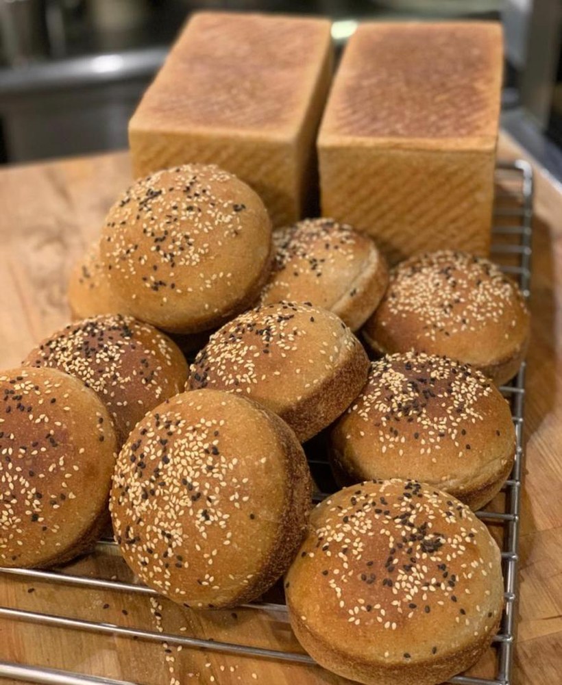 Sesame sourdough buns cooling on the rack, with two loaves behind
